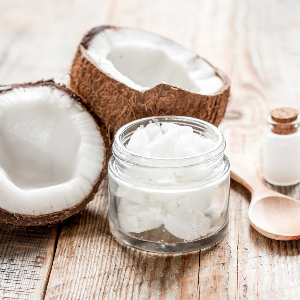 Relax Bath Salts product glass jar filled with coconut pieces with  fresh coconut halves, corked bottle with coconut oil, and wooden spoon  on wood surface