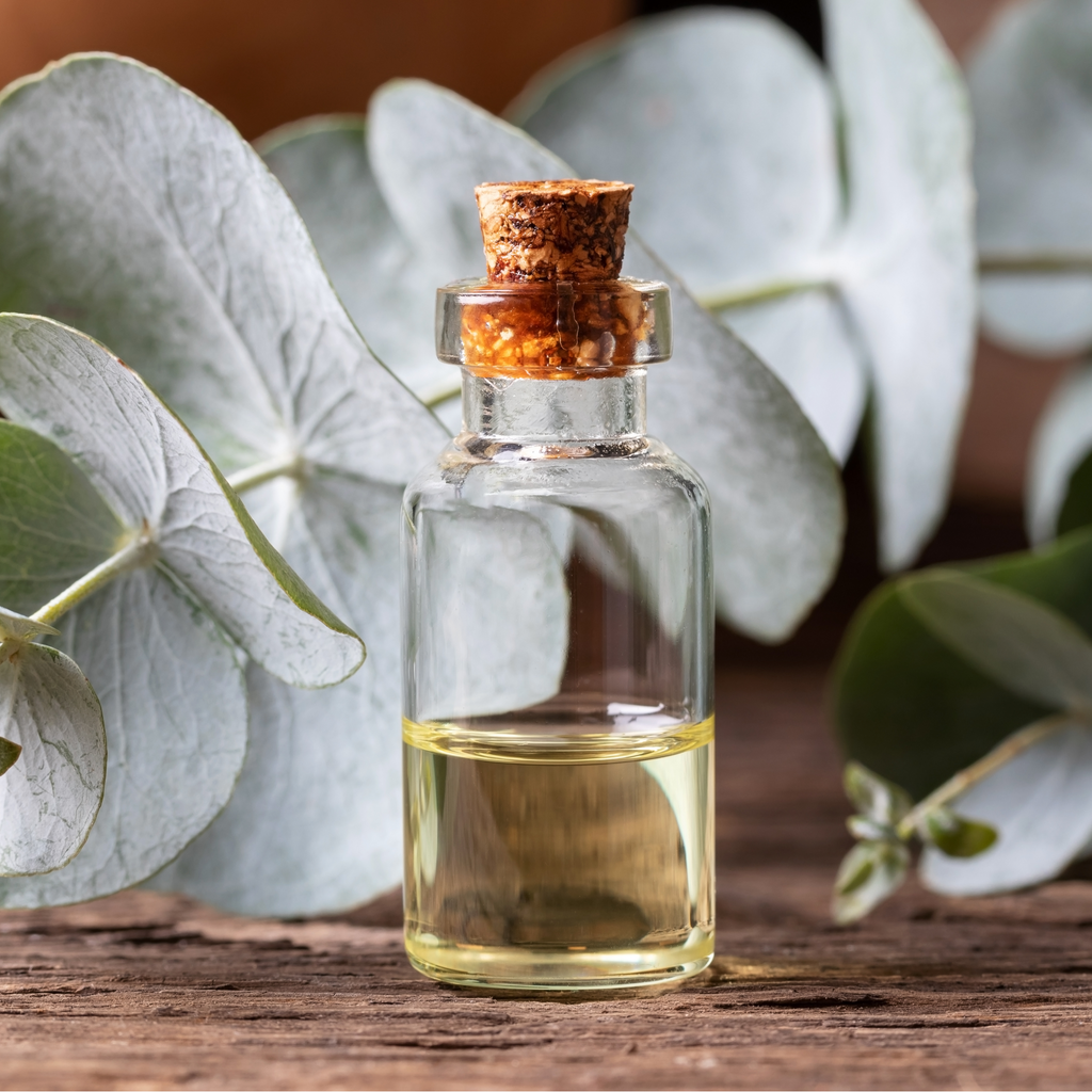 Rejuvenate Bath Salts glass bottle with cork stopper filled with oil, and eucalyptus sprig next to it, on wood surface