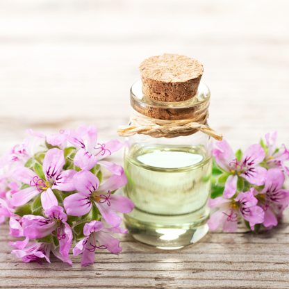 Menopause Bath Salts glass bottle with cork stopper and twine tied around neck filled with oil, and deep pink flowers next to it, on wood surface