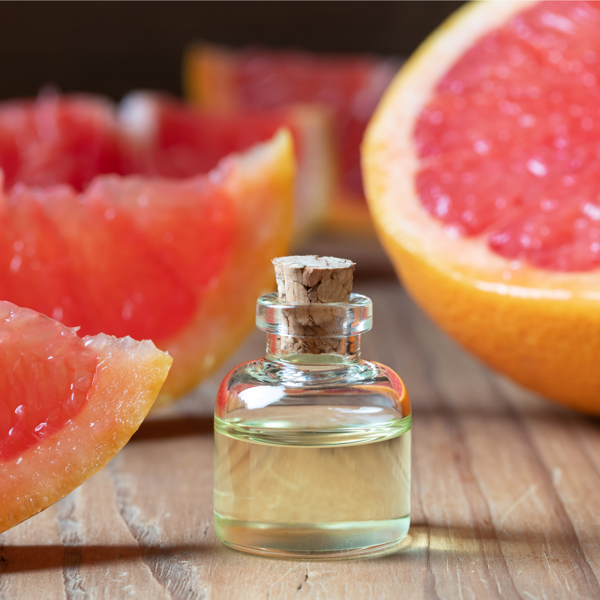 PMS Bath Salts glass bottle with cork stopper filled with oil, and sliced grapefruit next to it, on wood surface