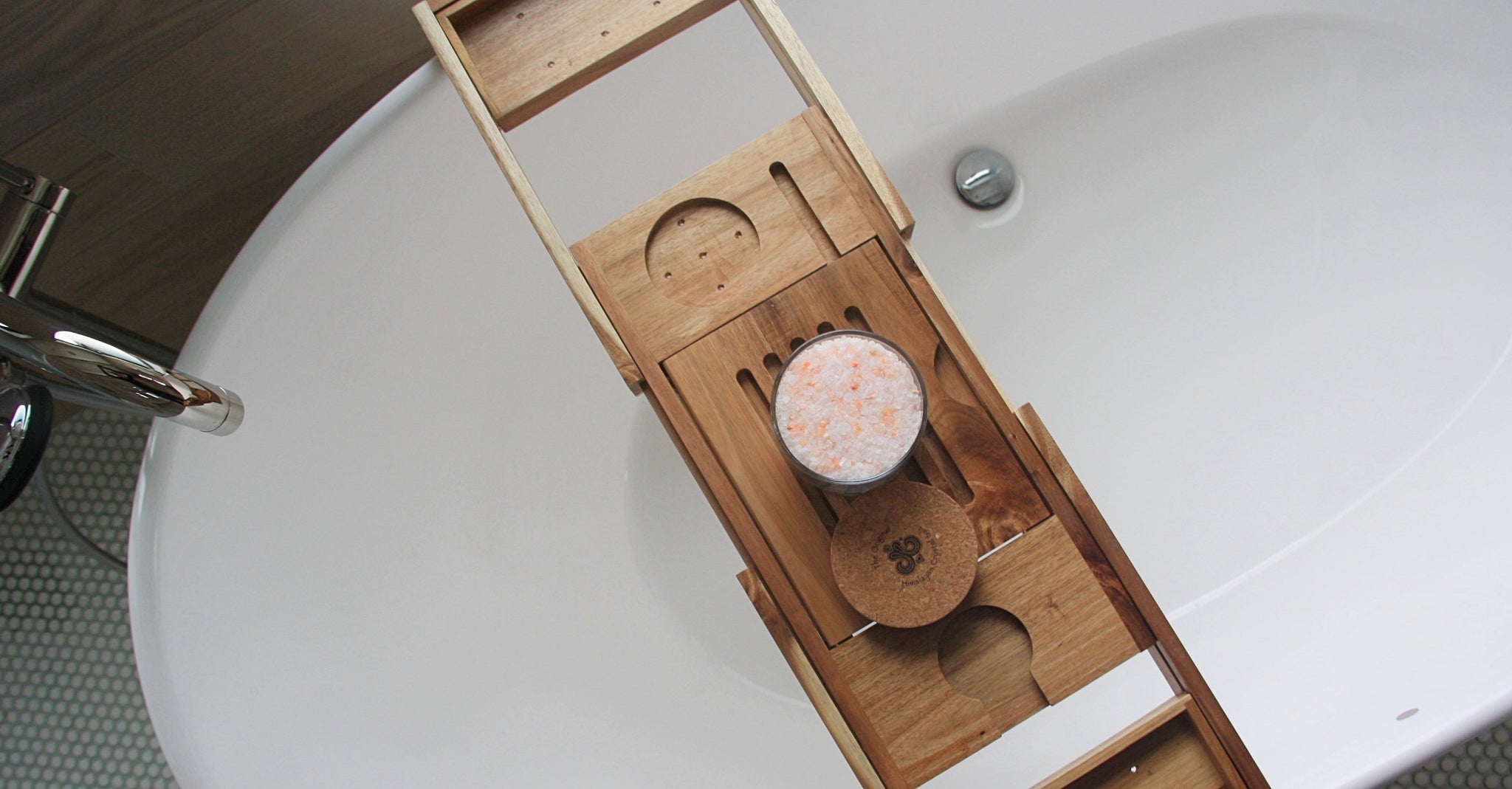 Rejuvenate Bath Salts product glass jar filled with Himalayan Crystal Salt, cork cover  resting on wooden tray with slats and candle holder groove resting on white tub in bathroom with window