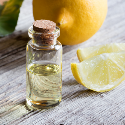 Detox Bath Salts glass bottle with cork stopper filled with oil, and whole and sliced lemon next to it, on bleached wood surface