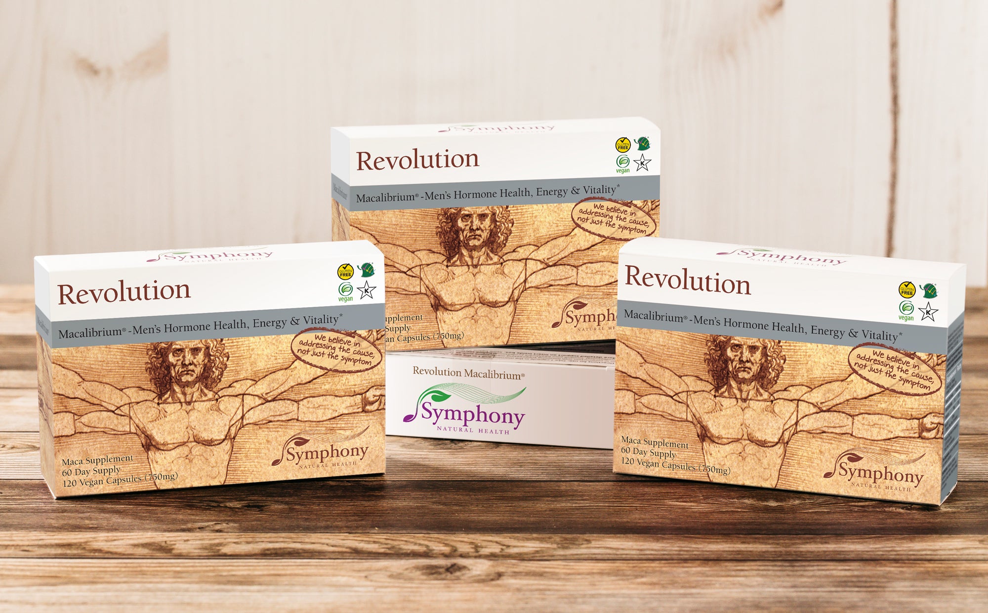 Revolution Macalibrium three product boxes, one elevated by another box laying on side, with Vitruvian Man illustration, we believe in addressing the cause not just the symptom, vegan, gluten free, Kosher, on light brown wood background