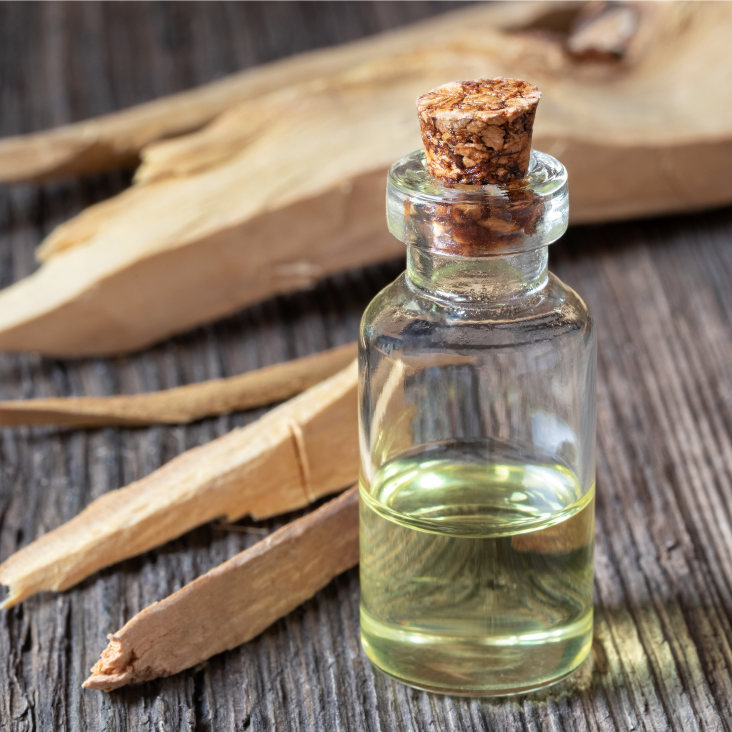 Relax Bath Salts glass bottle with cork stopper filled with oil, and sandalwood chips next to it, on dark wood surface