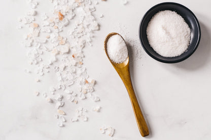 Fine Granulated Culinary Salt in black bowl and on brown wooden spoon with coarse salt on light gray marble counter