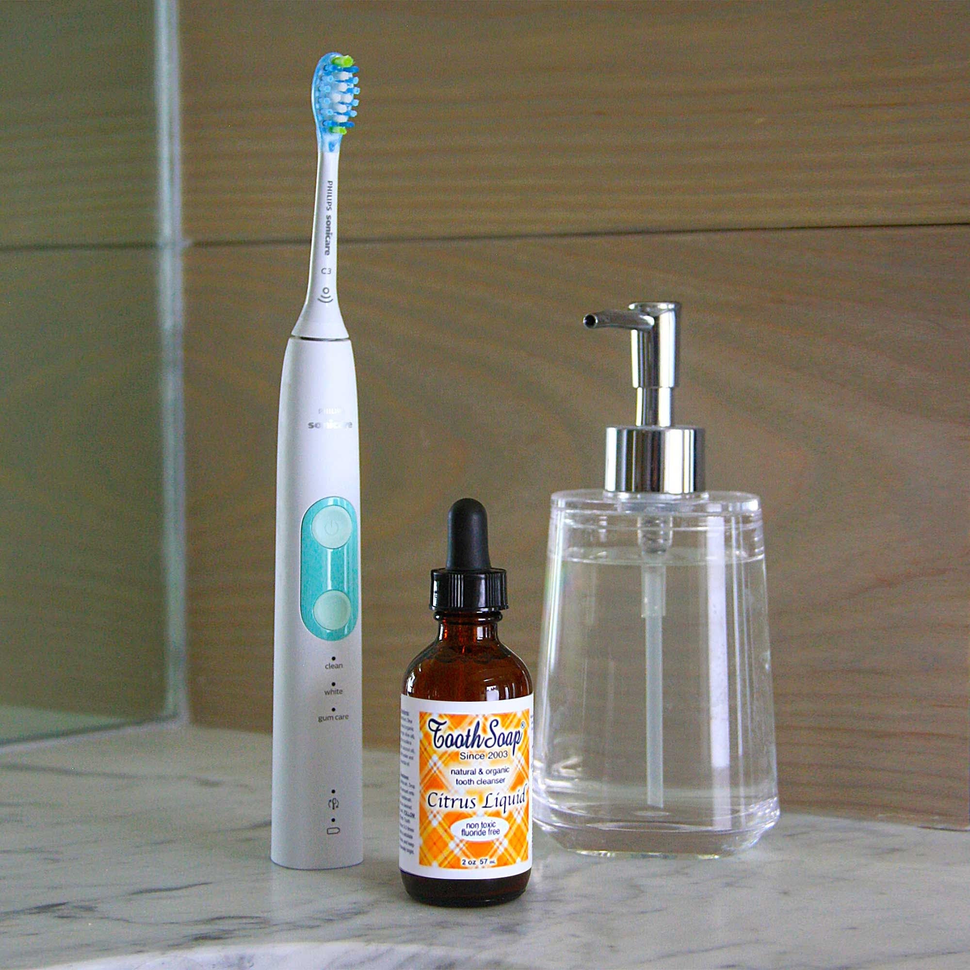 Citrus Tooth Soap white and turquoise standing electric toothbrush brown bottle with black dropper top, and orange and yellow label, clear glass dispenser