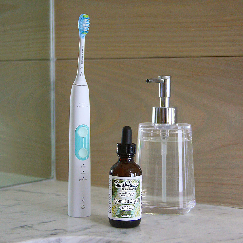 Spearmint Tooth Soap white and turquoise standing electric toothbrush brown bottle with black dropper top with green and white label, clear glass dispenser
